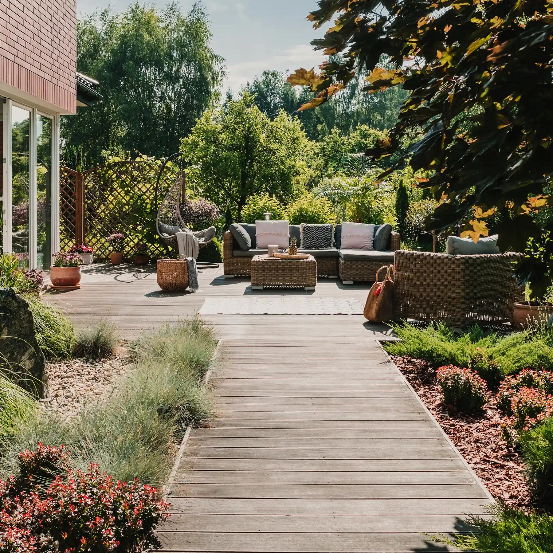 Holzterrasse mit Lounge Möbeln, Holzweg und dichter Bepflanzung in einem modern angelegten Garten.