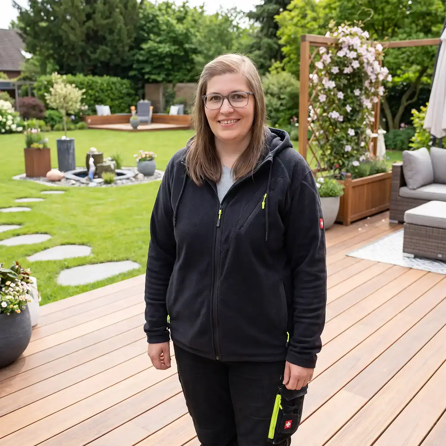 Fachkraft im Garten auf einer Holzterrasse mit gepflegtem Rasen, Lounge Bereich und moderner Gartengestaltung.